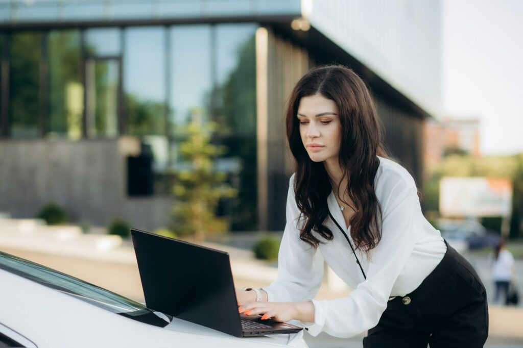 a businesswoman works on a laptop in the trunk of her own car