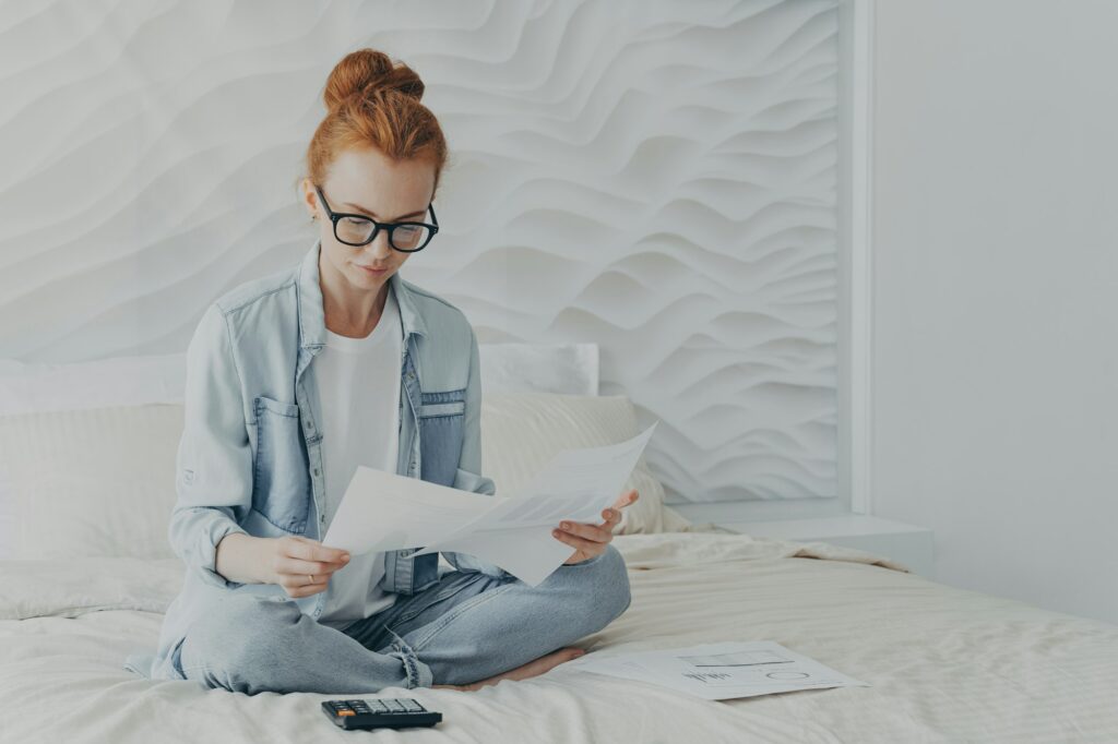 Beautiful ginger woman freelancer looks attentively at documents calculates manages finances